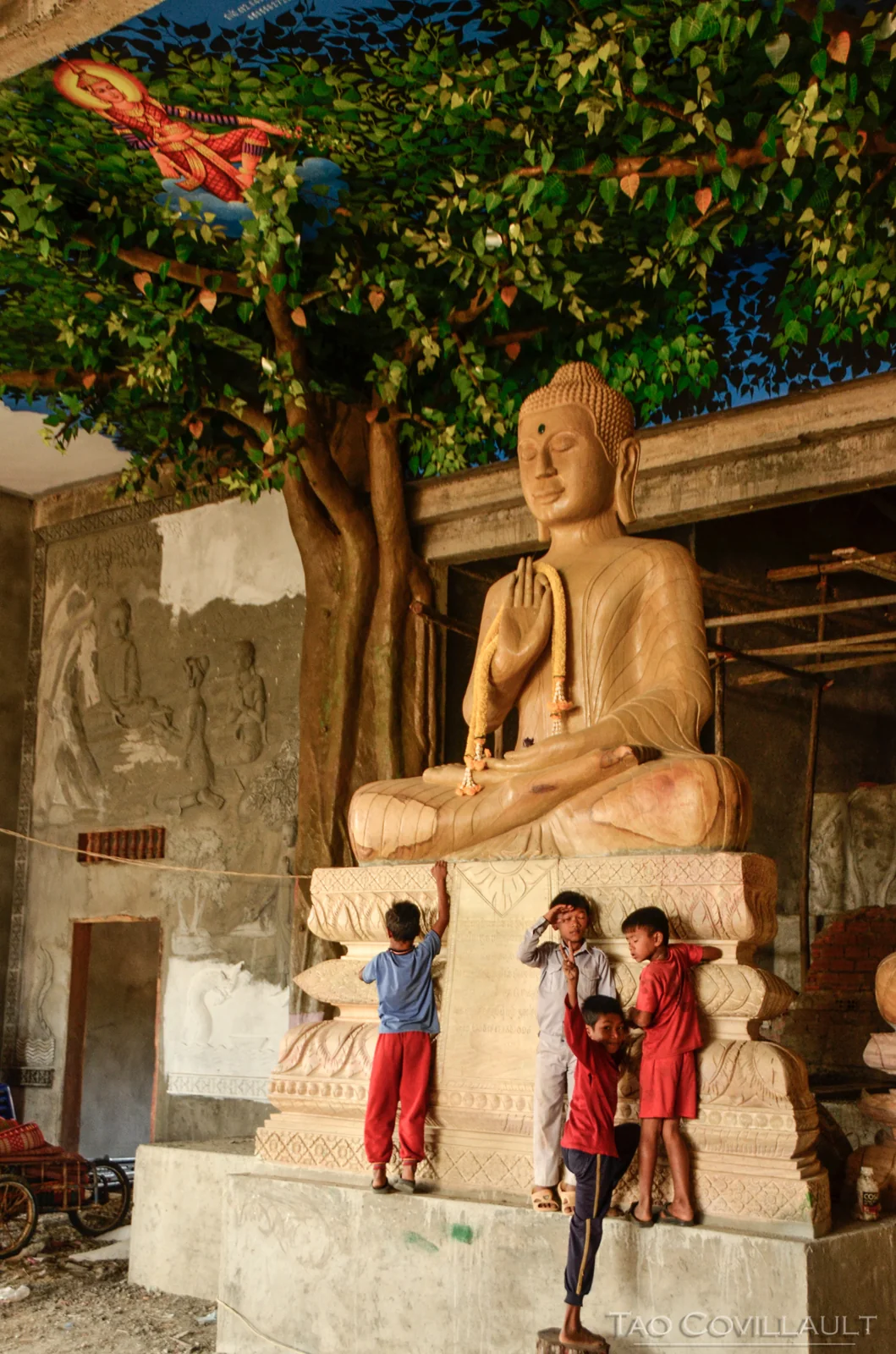 Children standing beneath a large seated Buddha statue.