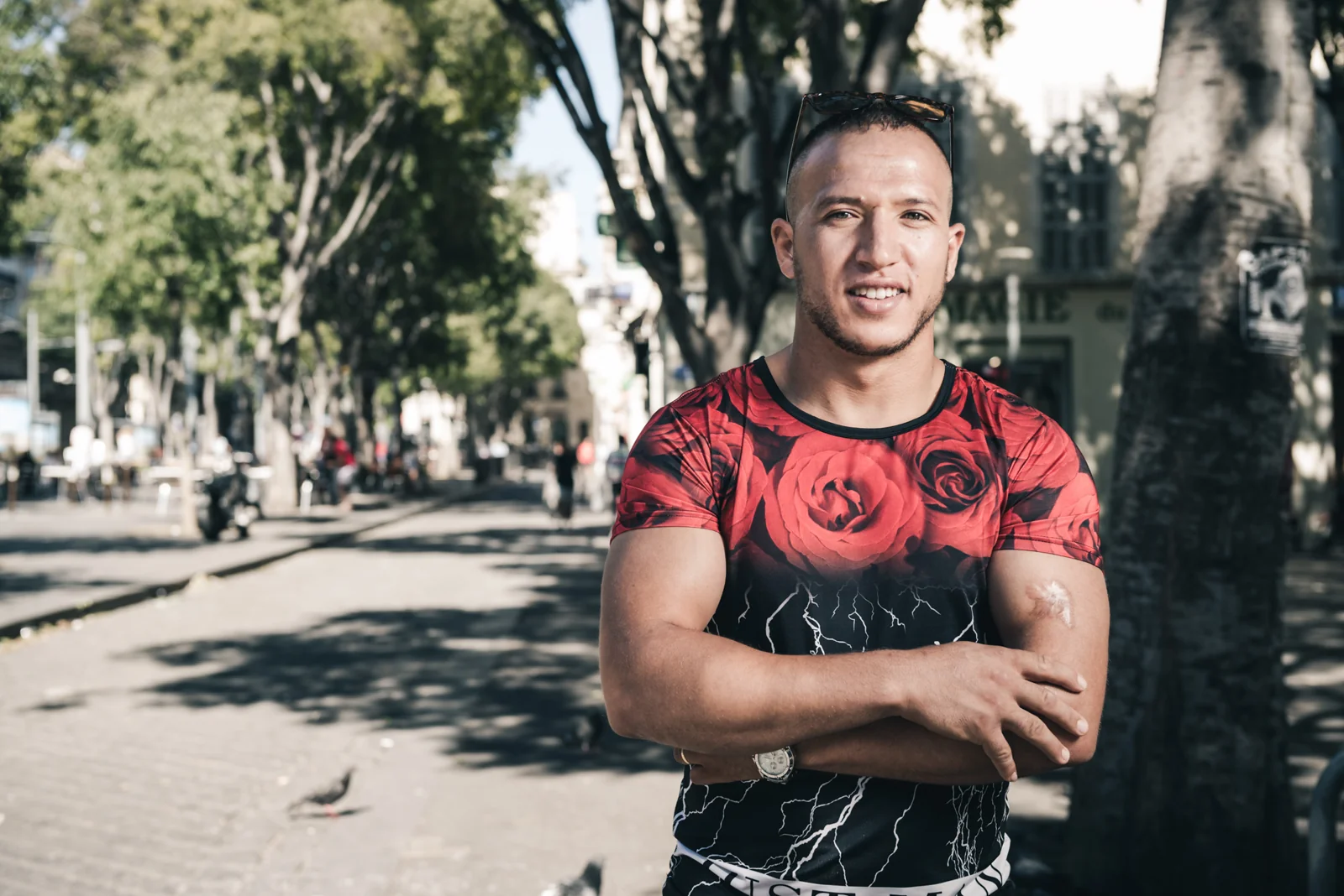 Man in a red and black shirt standing with folded arms.