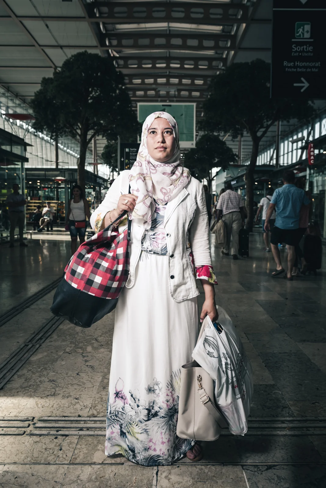 Woman in a patterned headscarf standing inside a railway station.