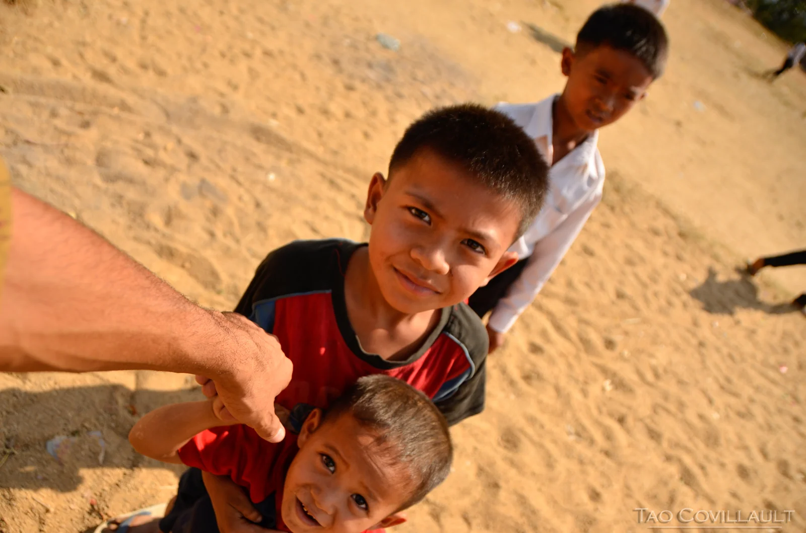 Children reaching toward the camera in a sandy courtyard.