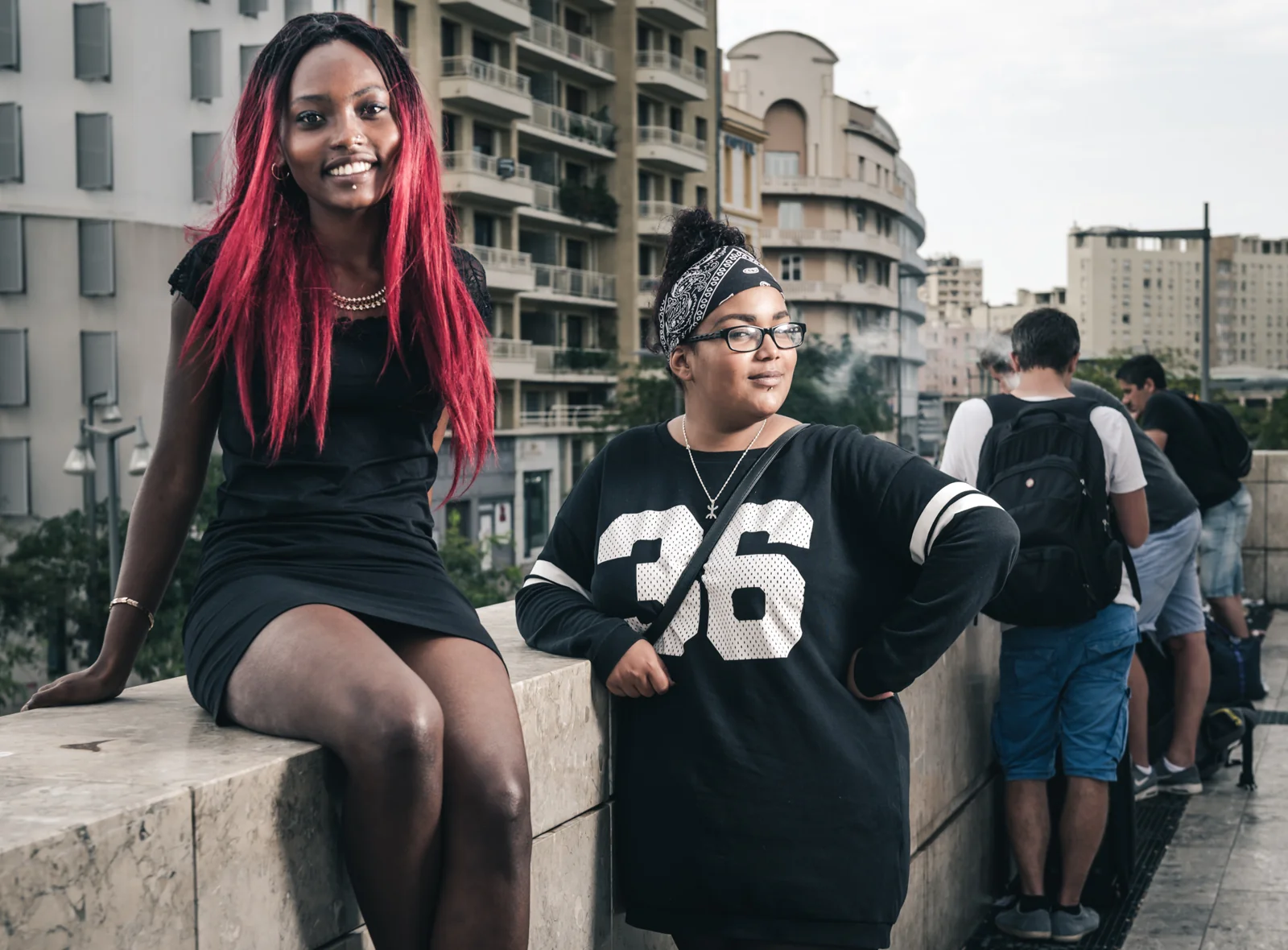 Two people posing beside a stone railing above a city street.