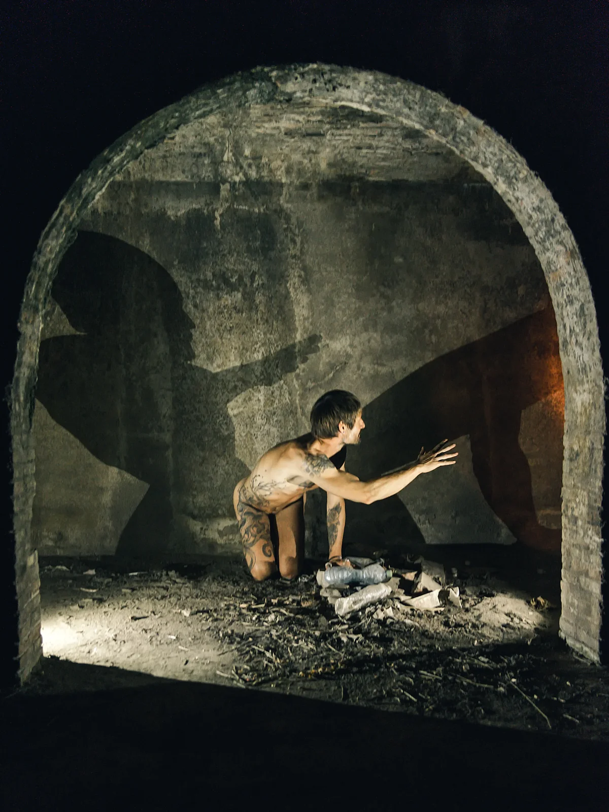 Fine-art nude figure crouching low with one arm extended toward a wall.