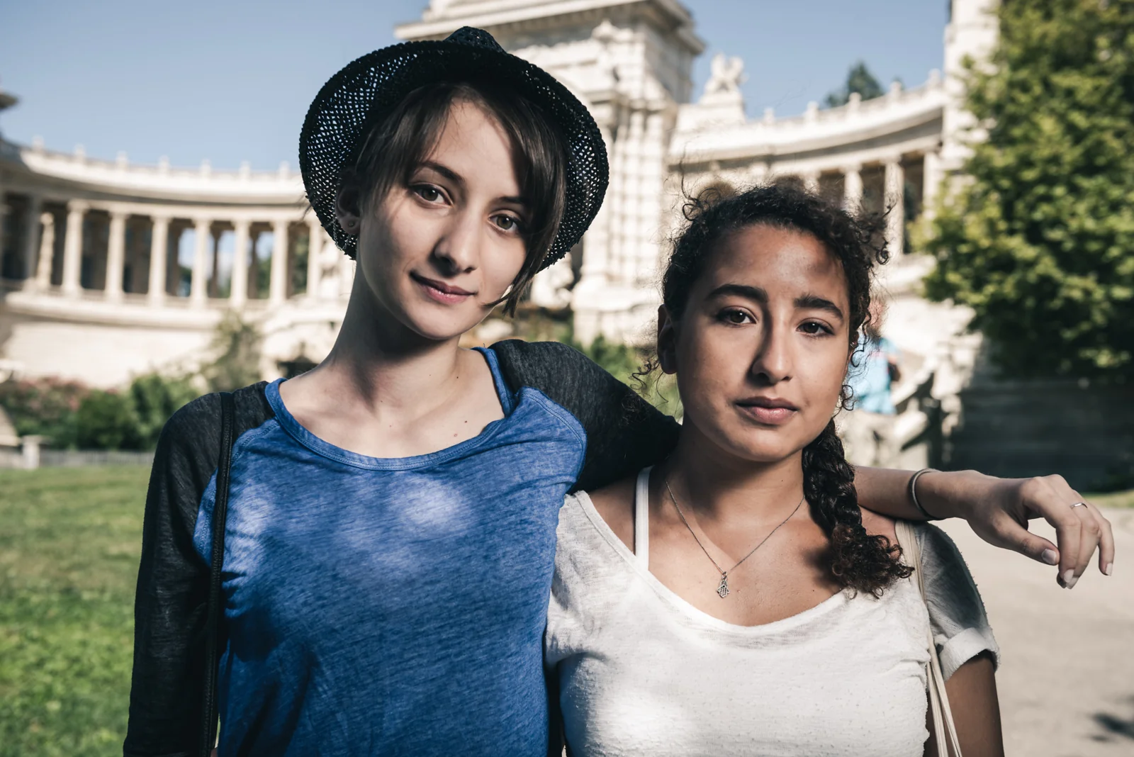 Two people posing closely together in front of a stone colonnade.