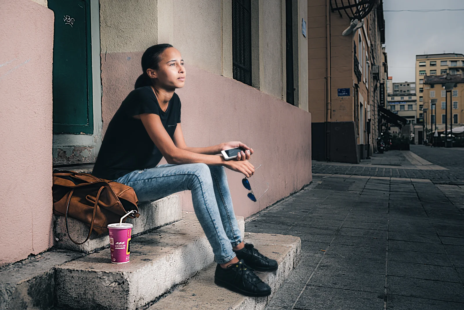 Woman seated on a doorstep beside a drink and handbag.
