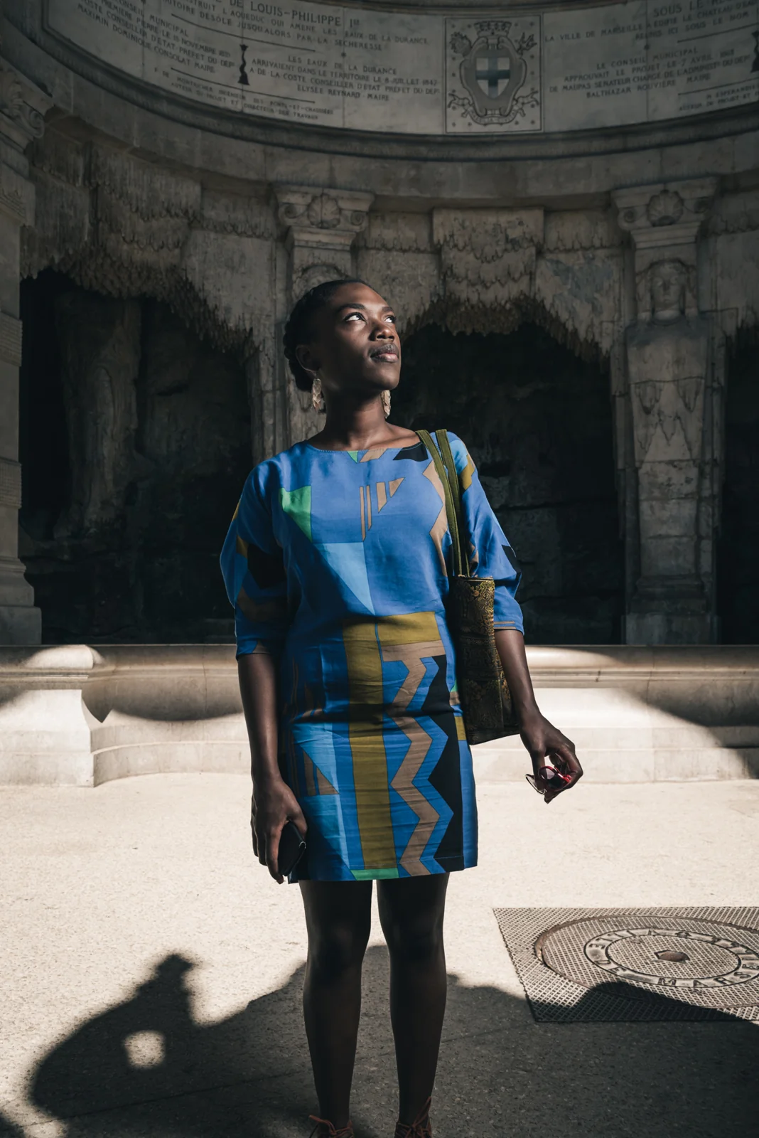 Woman in a blue patterned dress beneath a stone archway.