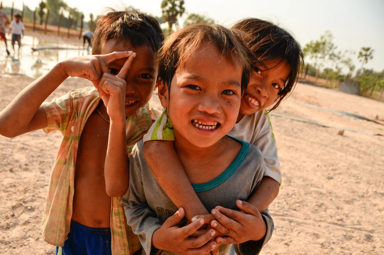Smiling children leaning together near the water.
