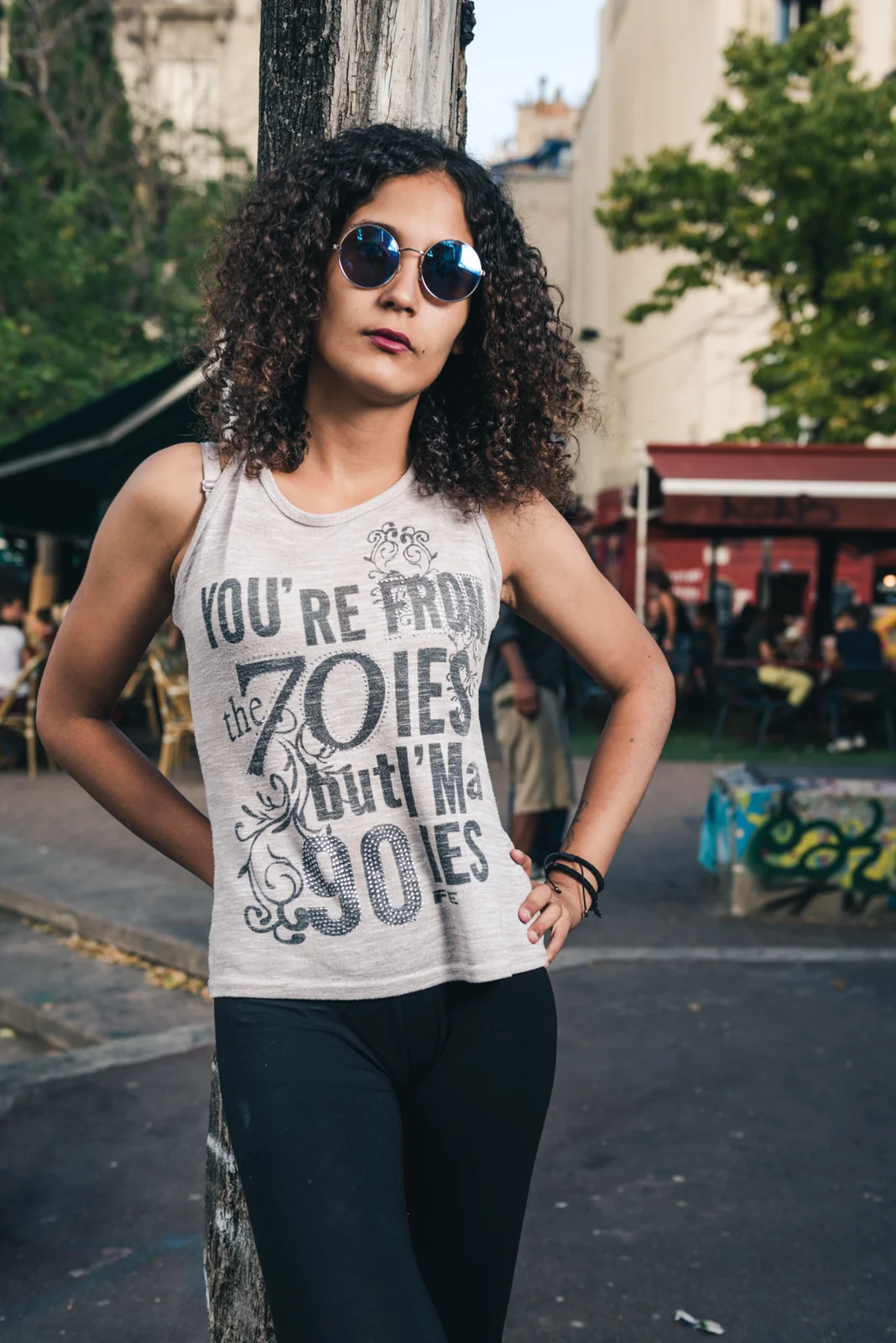 Woman with curly hair and sunglasses standing with hands on hips.
