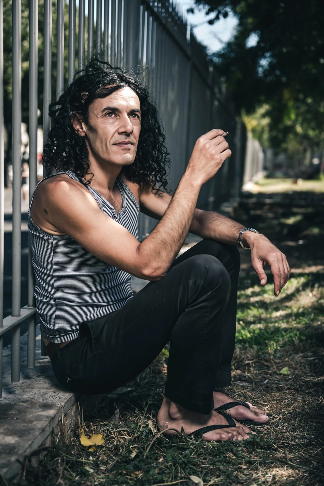 Man with long dark hair seated beside an iron fence.