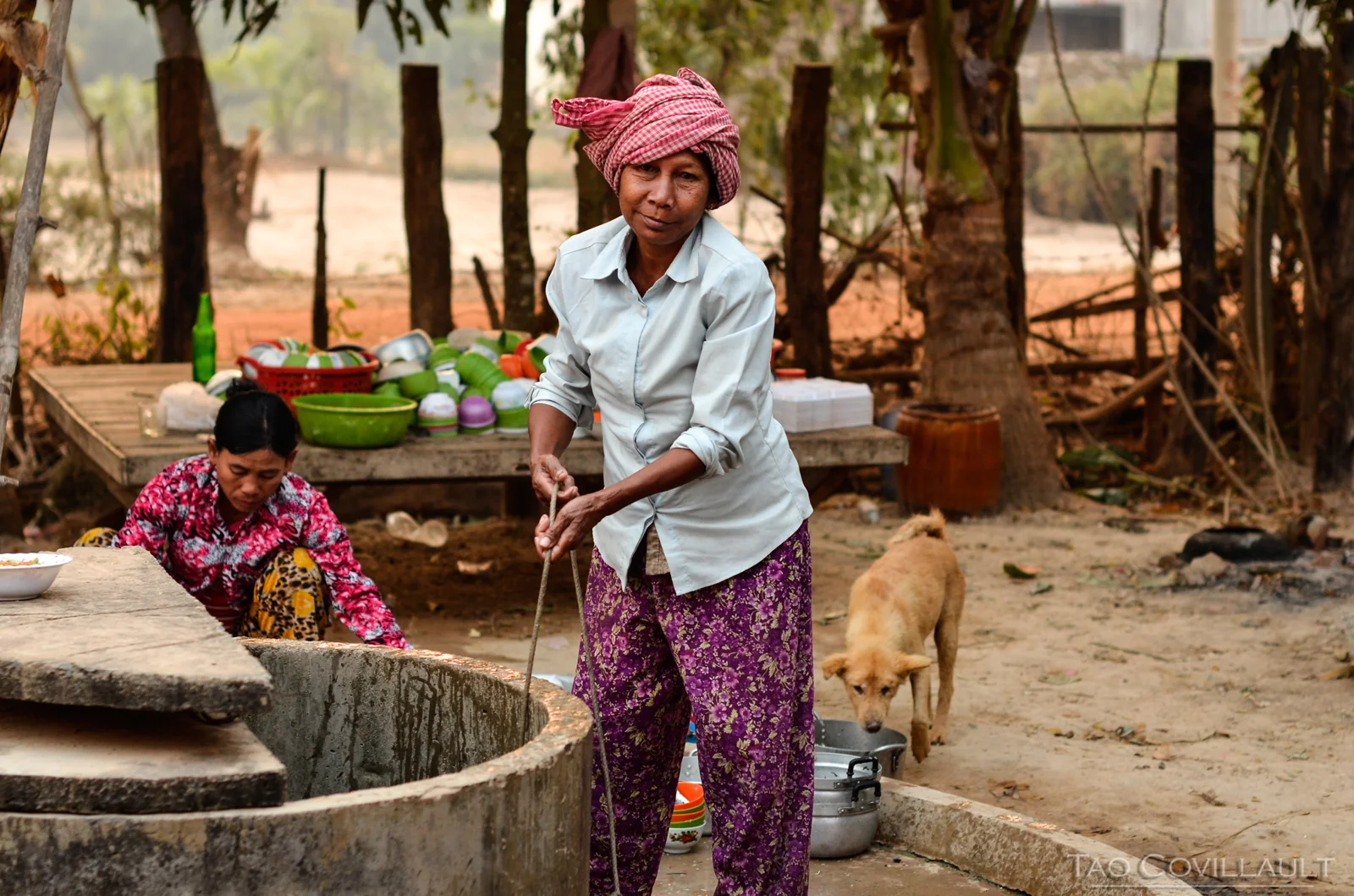 Woman drawing water beside an outdoor well.