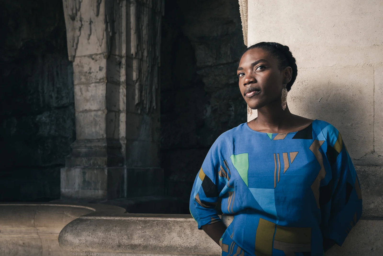 Portrait of a woman in a blue patterned dress beside a stone column.