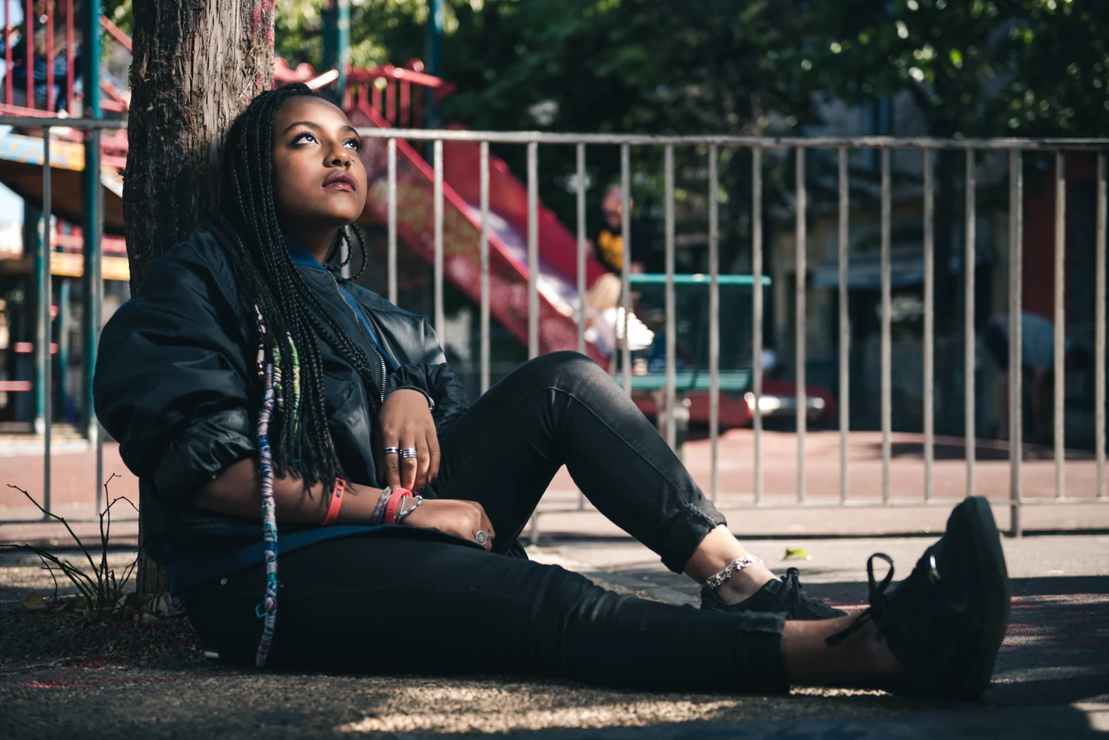 Woman seated in the shade beside a playground fence.
