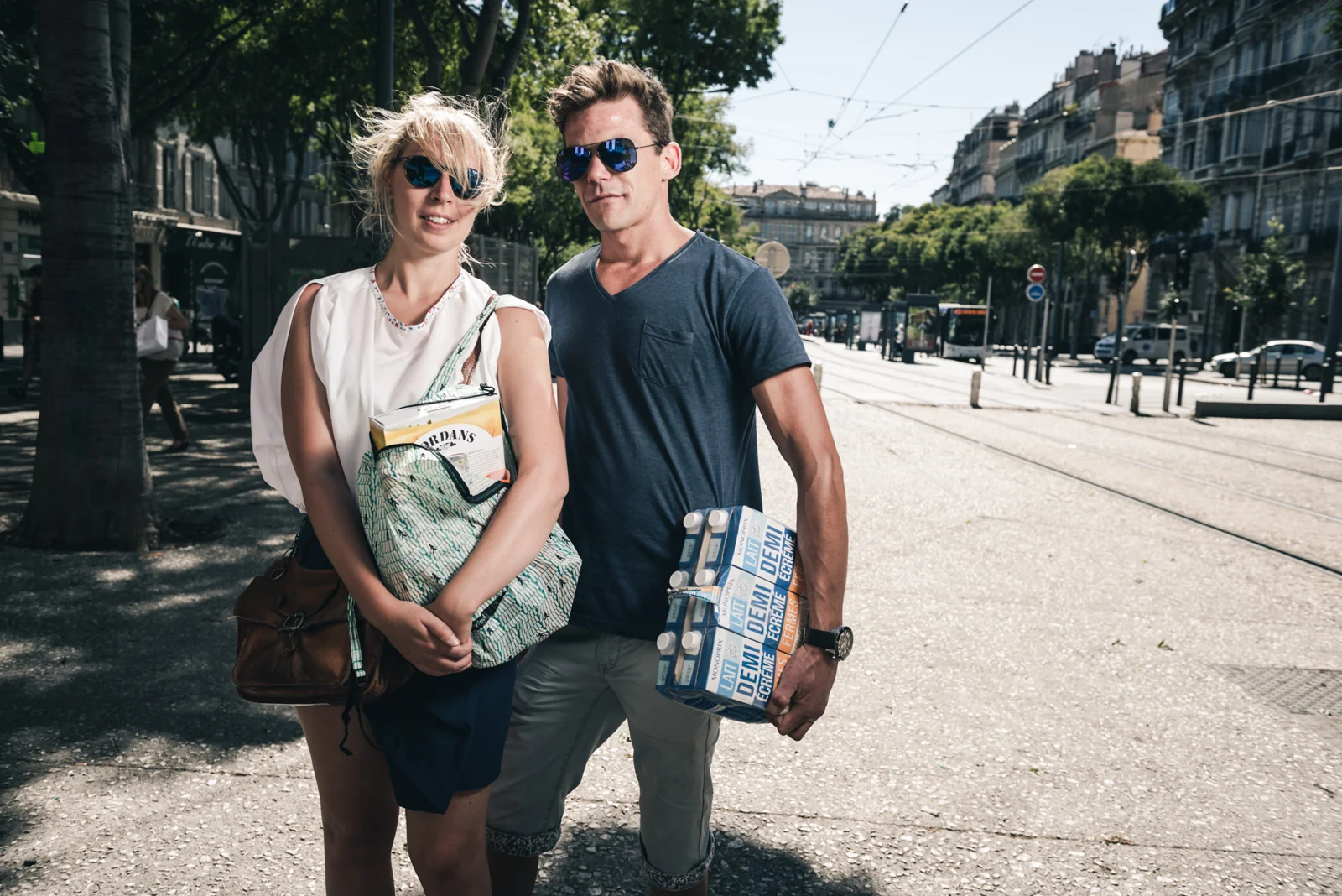 Two visitors in sunglasses standing together on a broad city street.