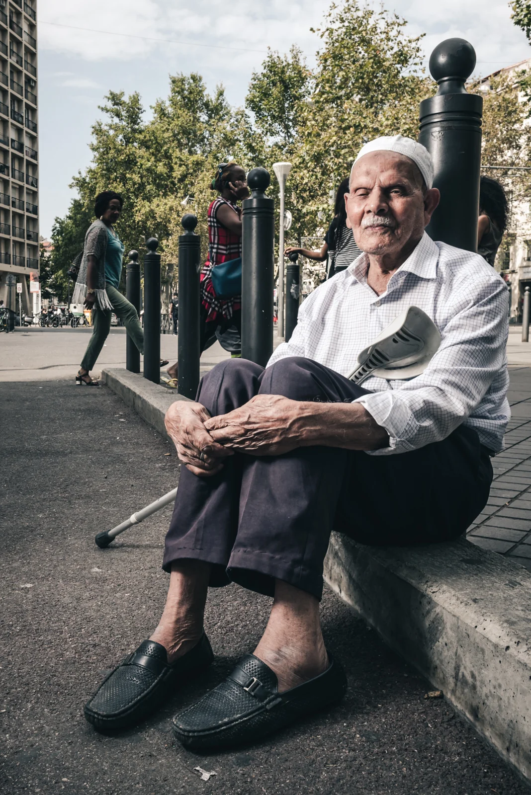 Older man seated on a low wall beside a city path.