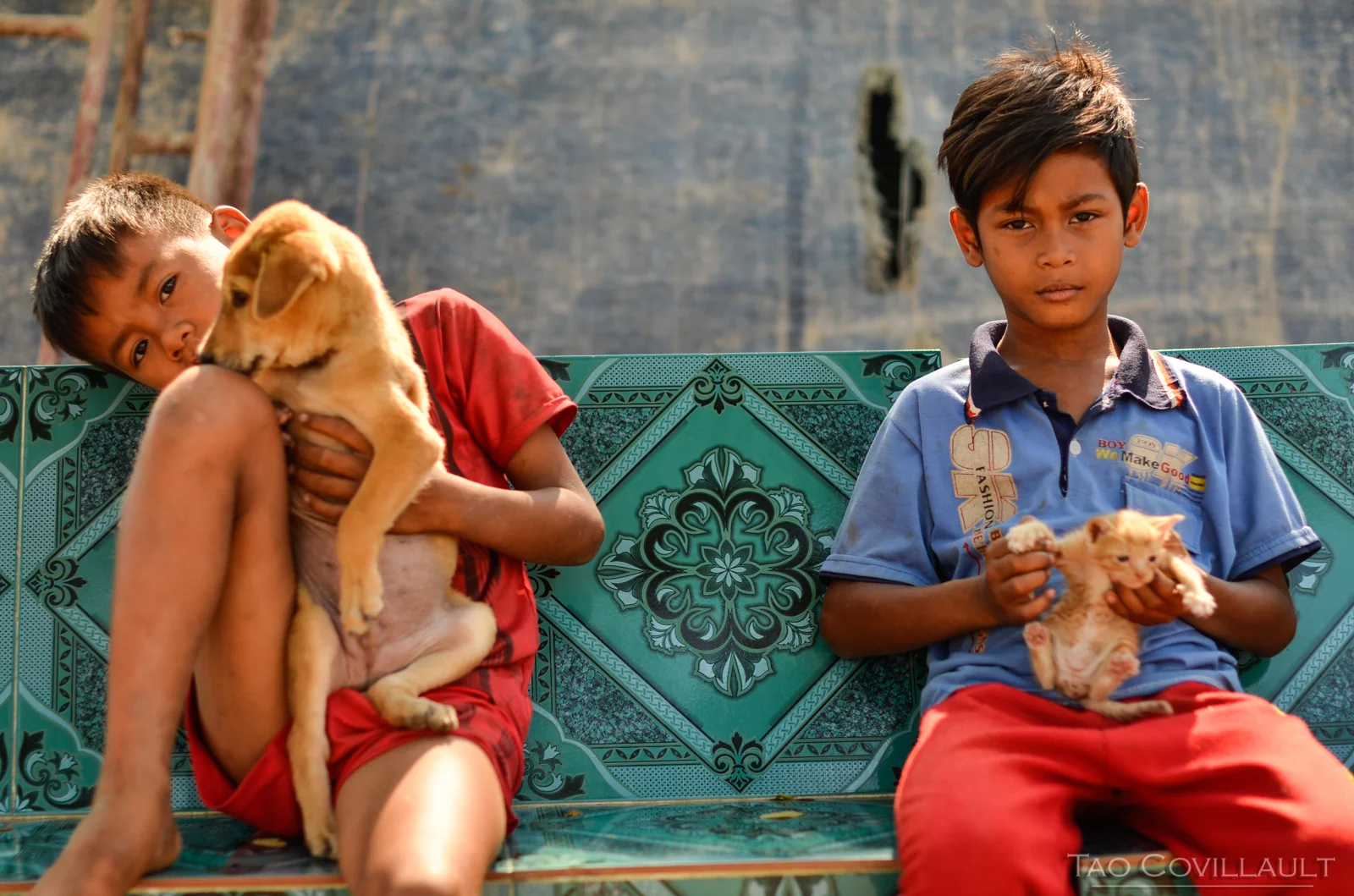 Two children seated on a patterned bench, one holding a puppy.