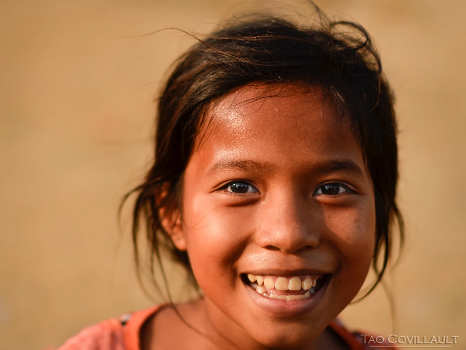 Close portrait of a smiling child against a warm plain background.