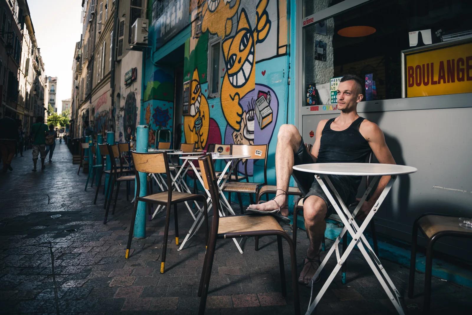 Person seated at a small café table on a narrow street.
