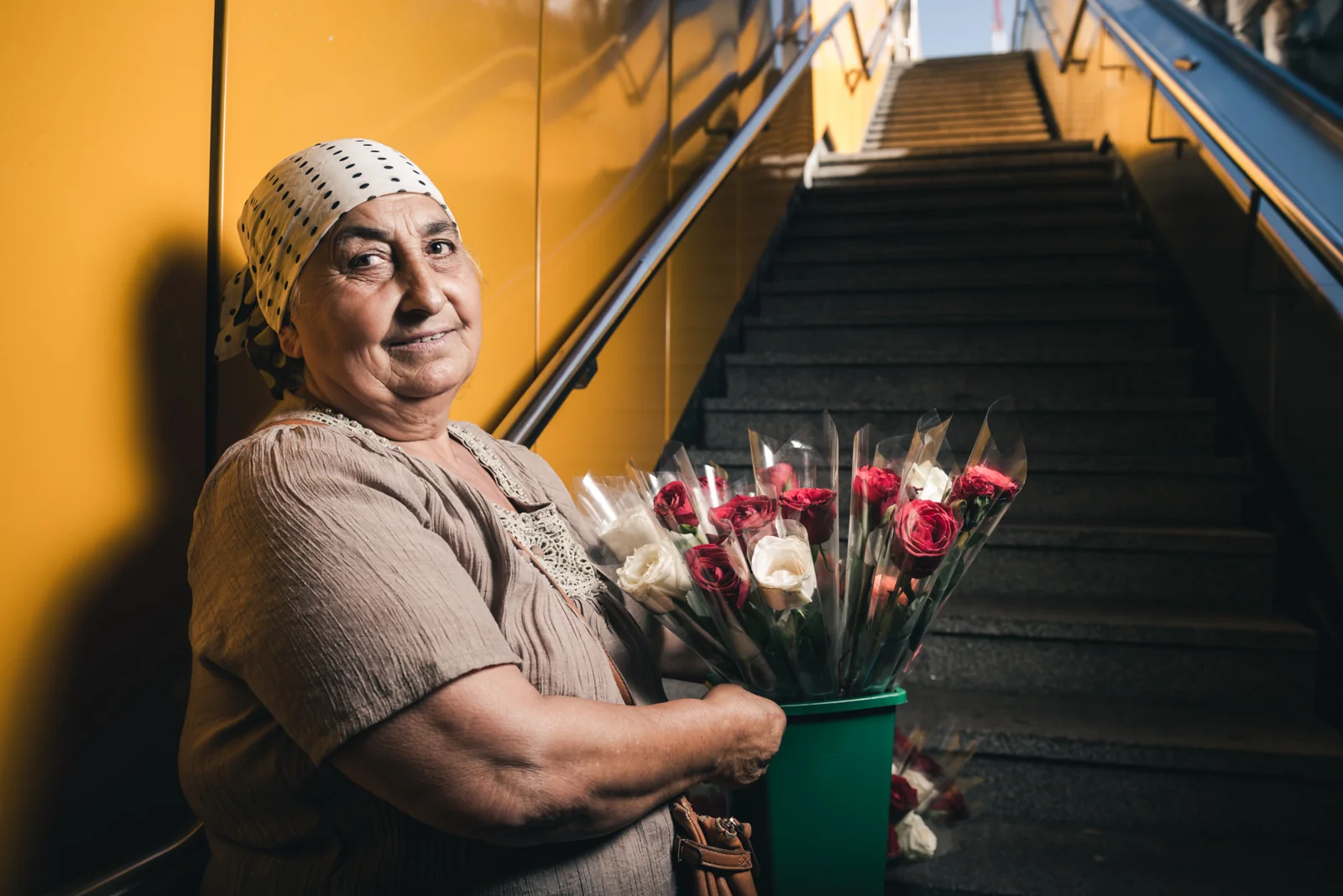 Man holding red roses beside a yellow stairwell.