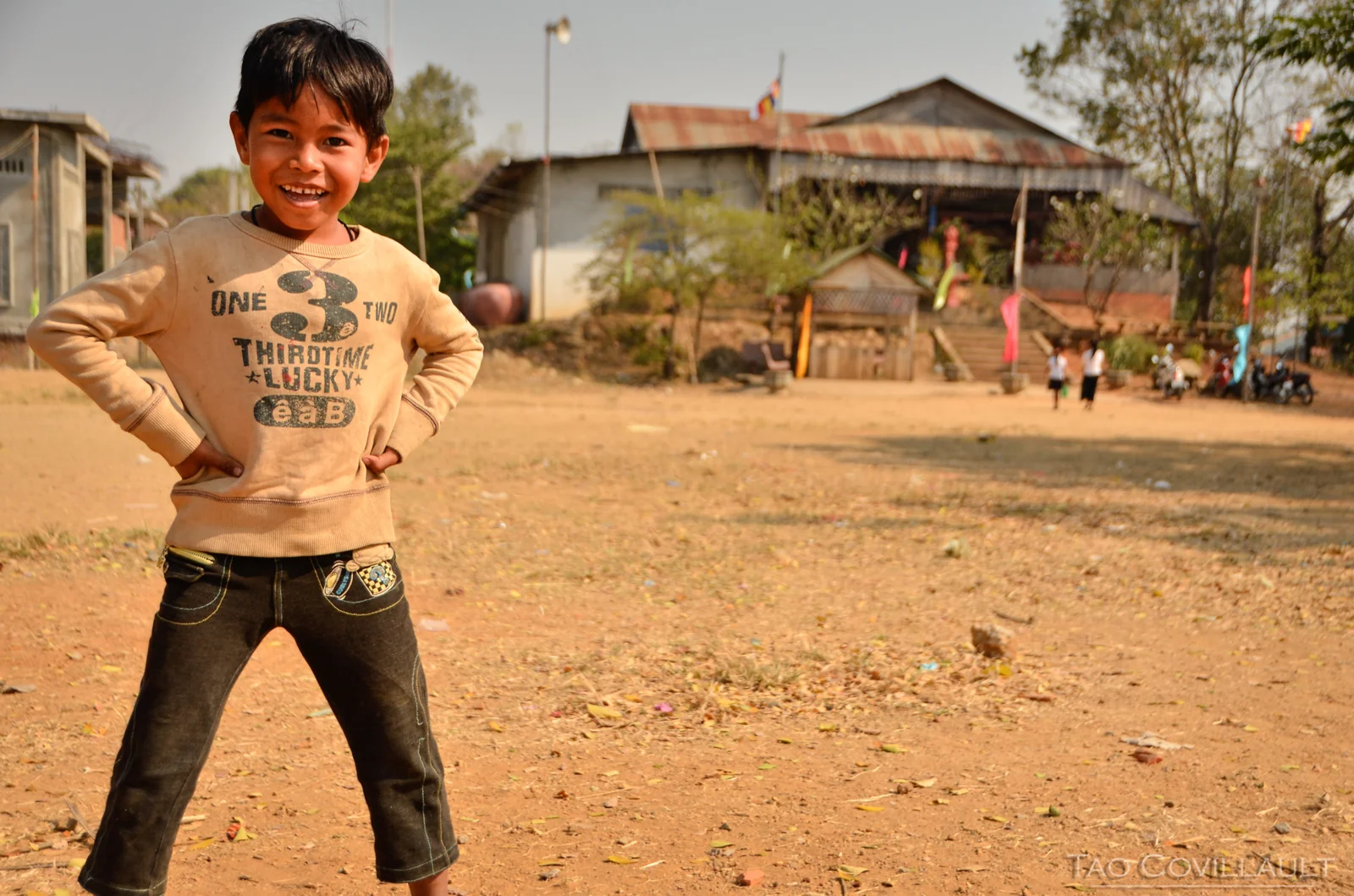 Child posing with hands on hips in an open village courtyard.