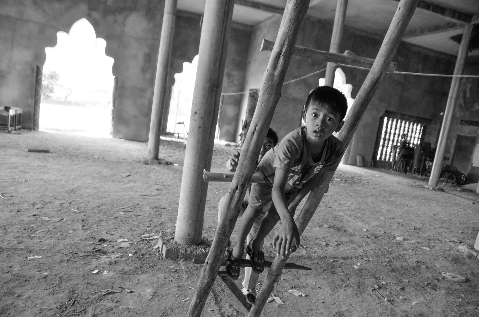 Black-and-white view of a child climbing wooden scaffolding inside a temple.