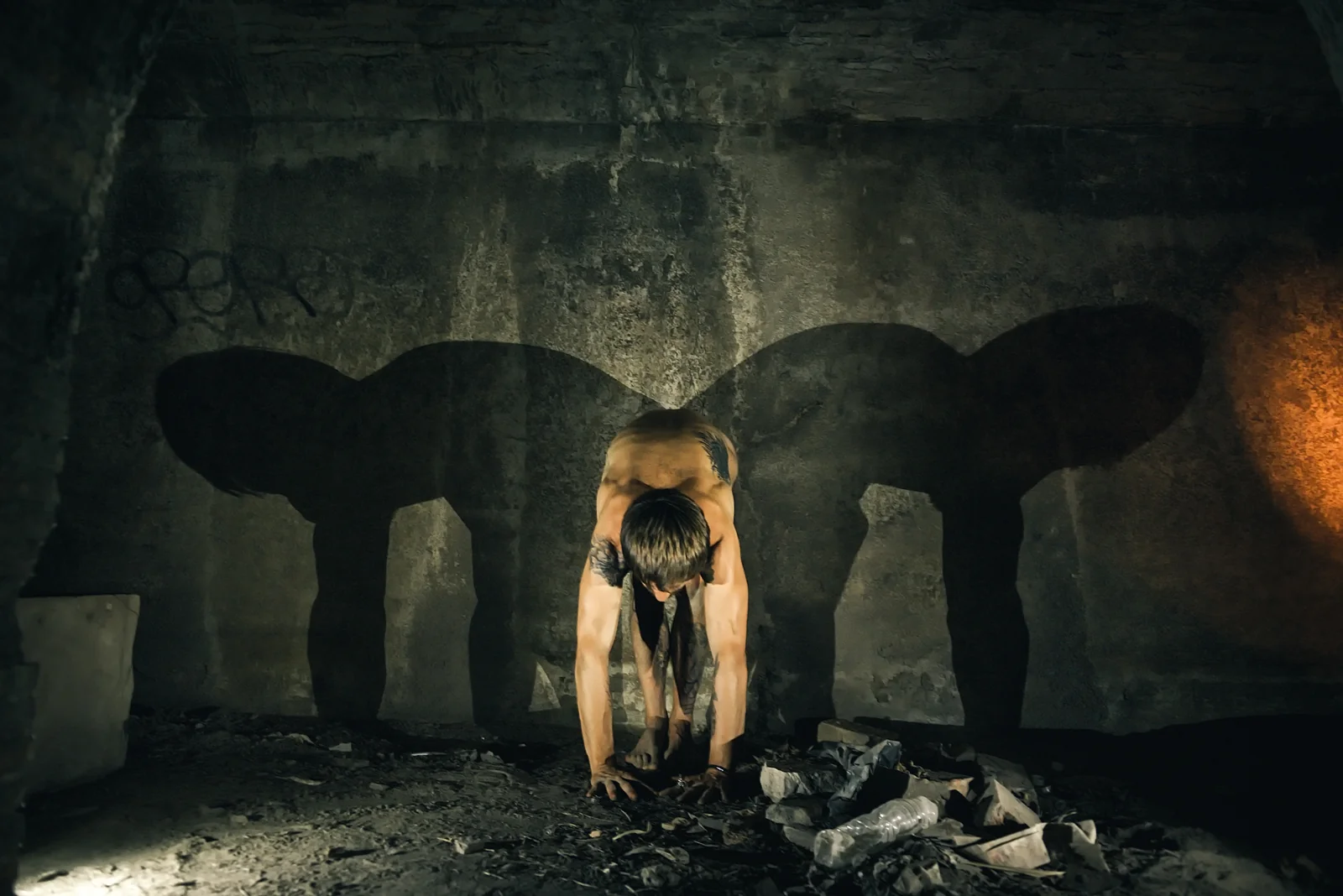 Fine-art nude figure bending forward between two broad wall shadows.