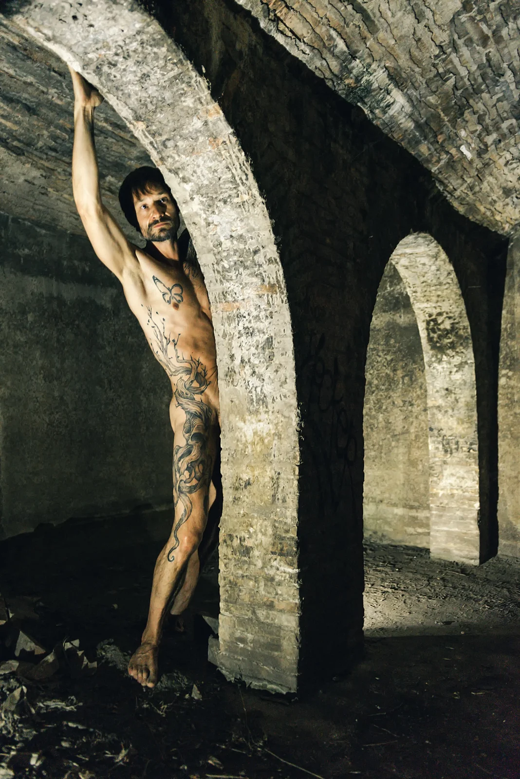 Fine-art nude figure stretching upward beneath a rough stone arch.