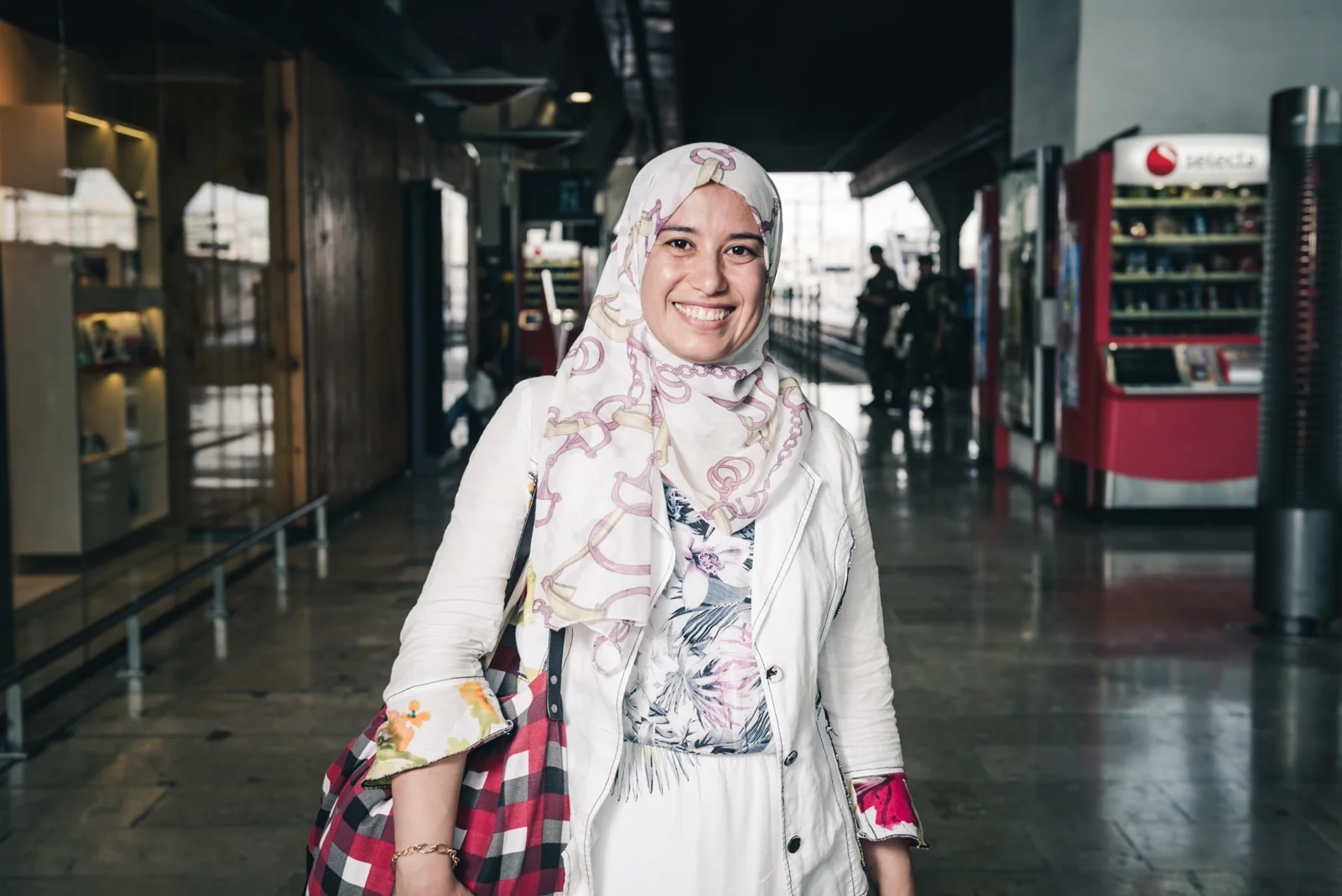 Smiling woman in a patterned headscarf inside a railway station.