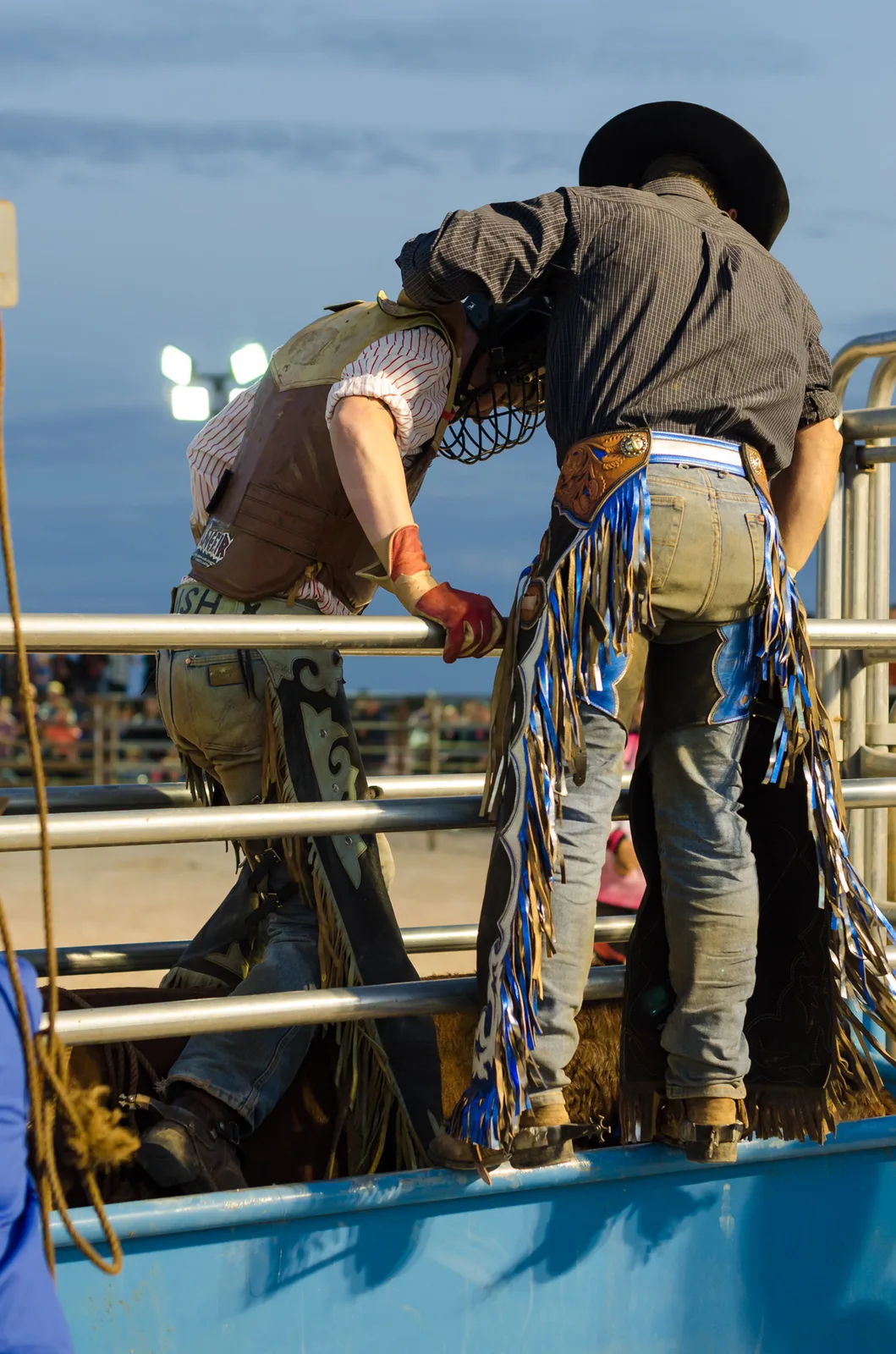 Rodeo participant standing on arena railings in patterned chaps.