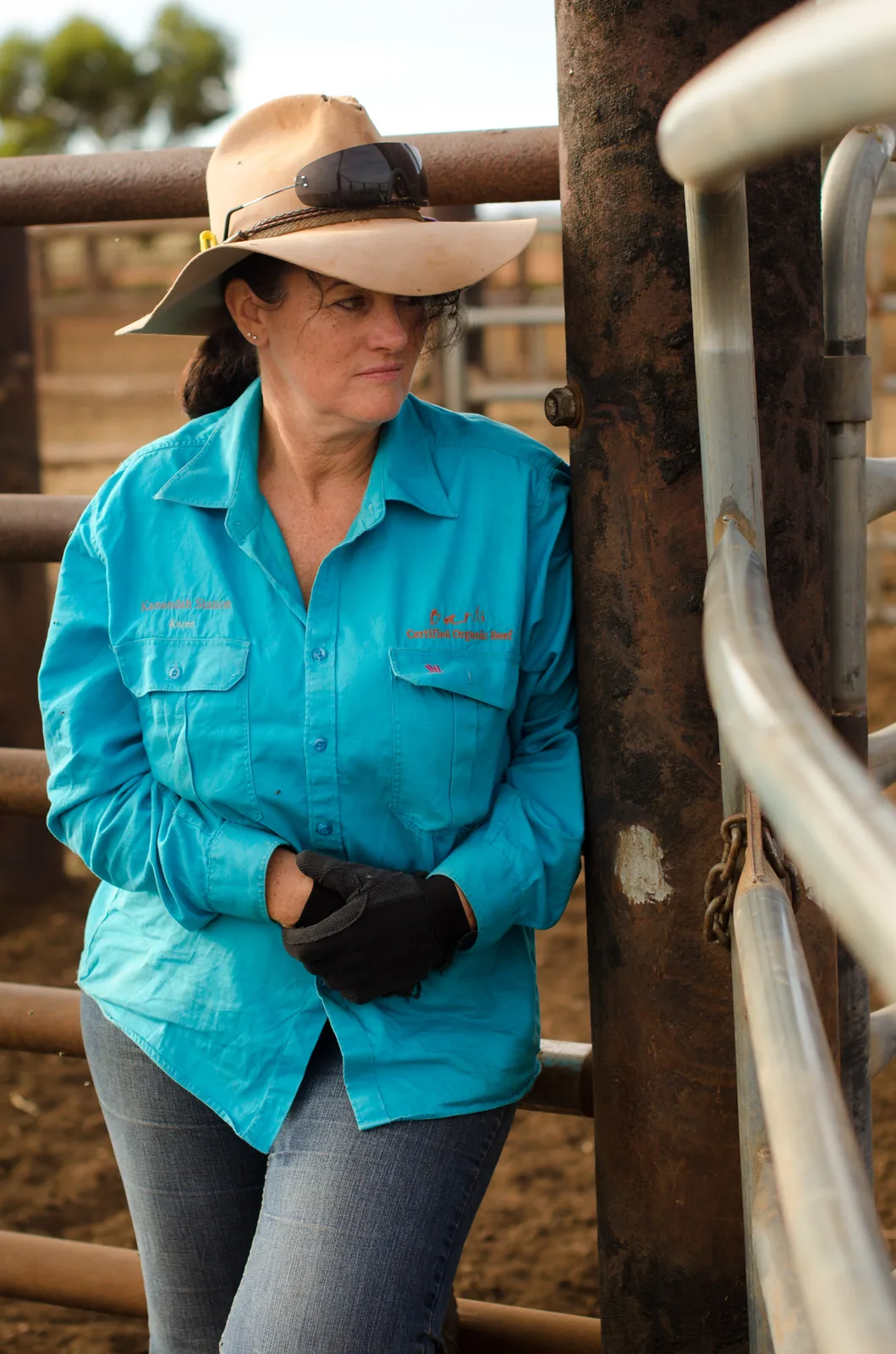 Stockwoman in a turquoise shirt and straw hat beside a gate.
