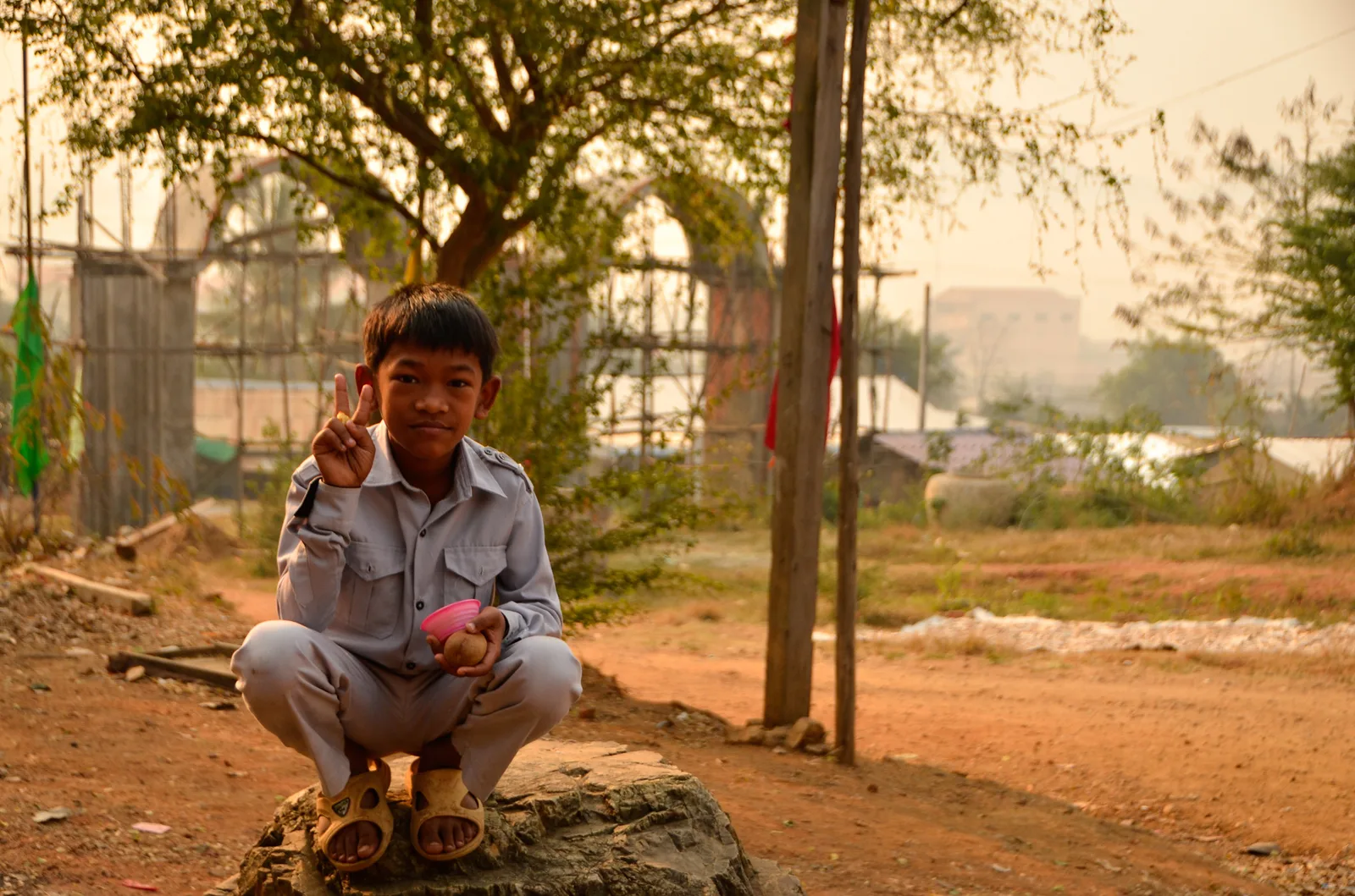Child crouching on a stone beneath trees.