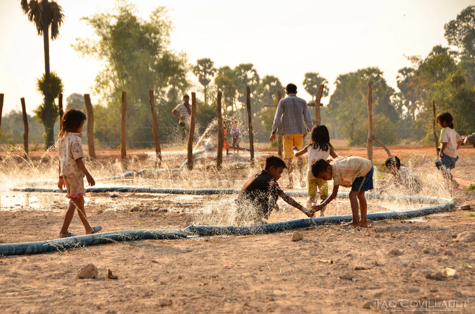 Children playing in spraying water beside a hose.