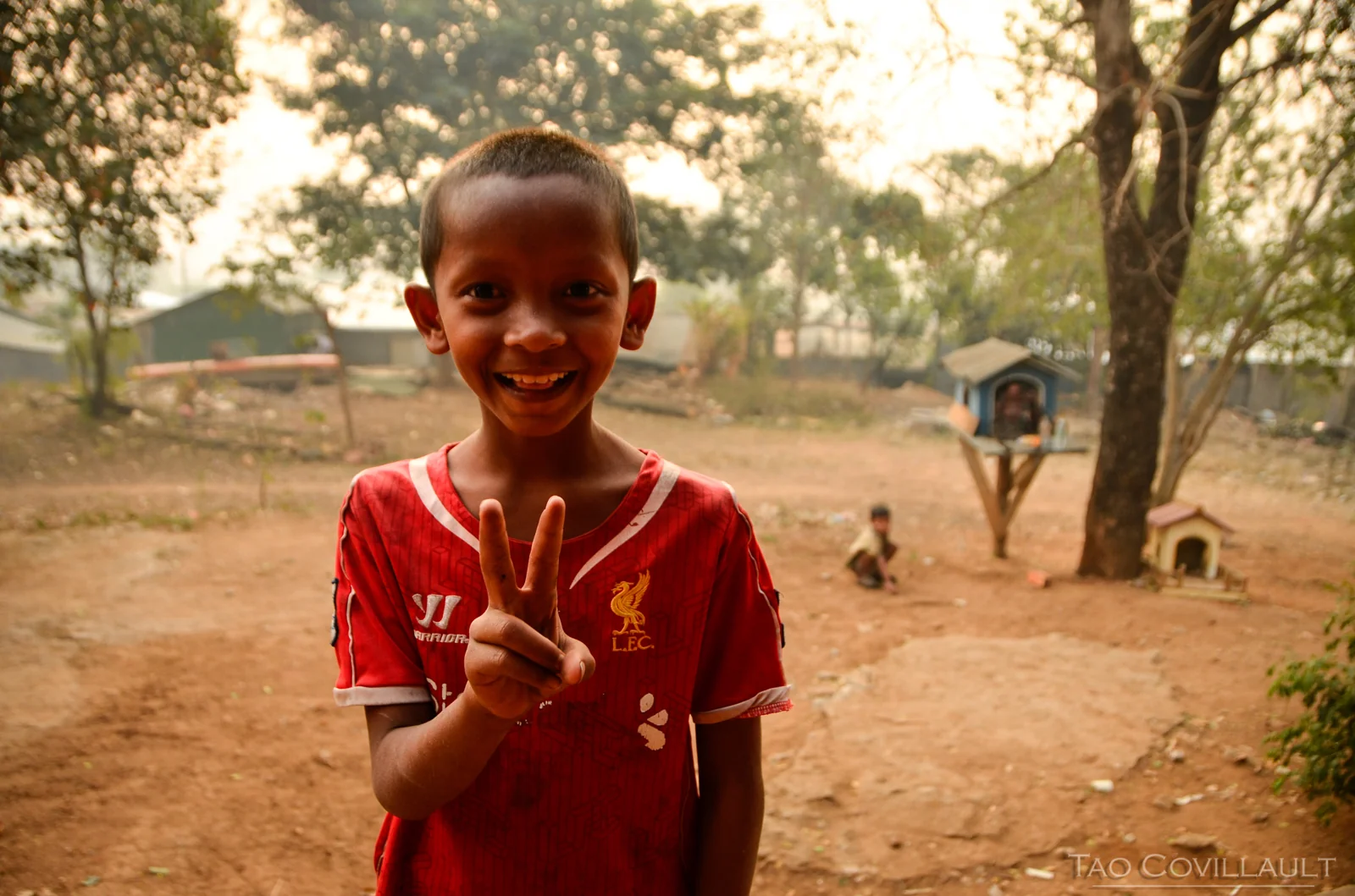 Smiling child in a red football shirt making a hand gesture.