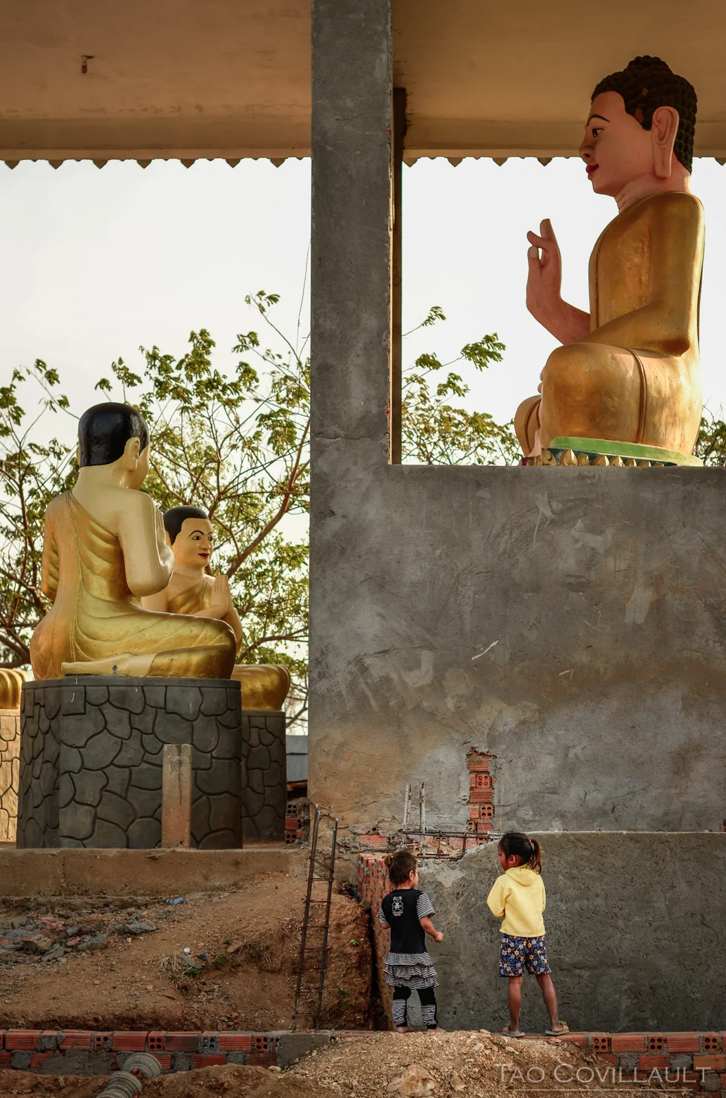 Children standing below large Buddha statues in a temple.