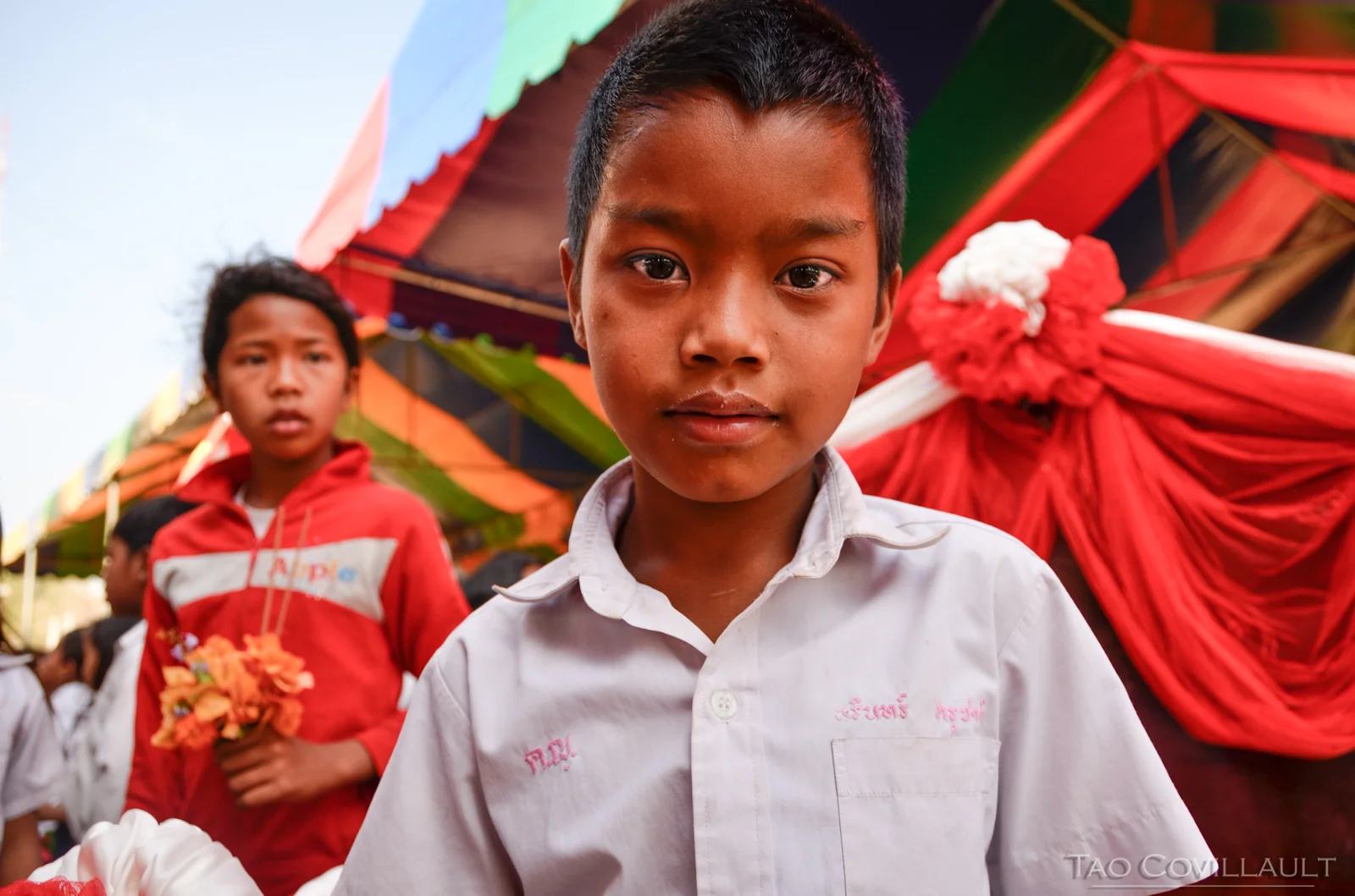 Child in a white shirt in front of colorful temple decorations.